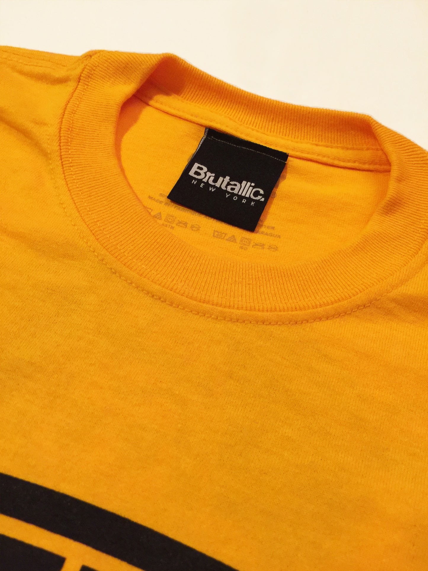 Brutallic Streetwear bubble tee tshirt with oval front logo, and buddha on the back, mustard yellow color, close up of neck collar label